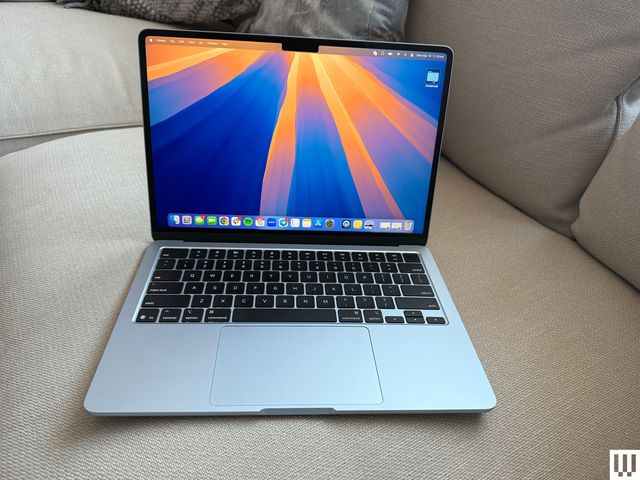 Front view of an open Apple MacBook Air 13-inch 2025  laptop sitting on a couch with the screen showing the desktop 