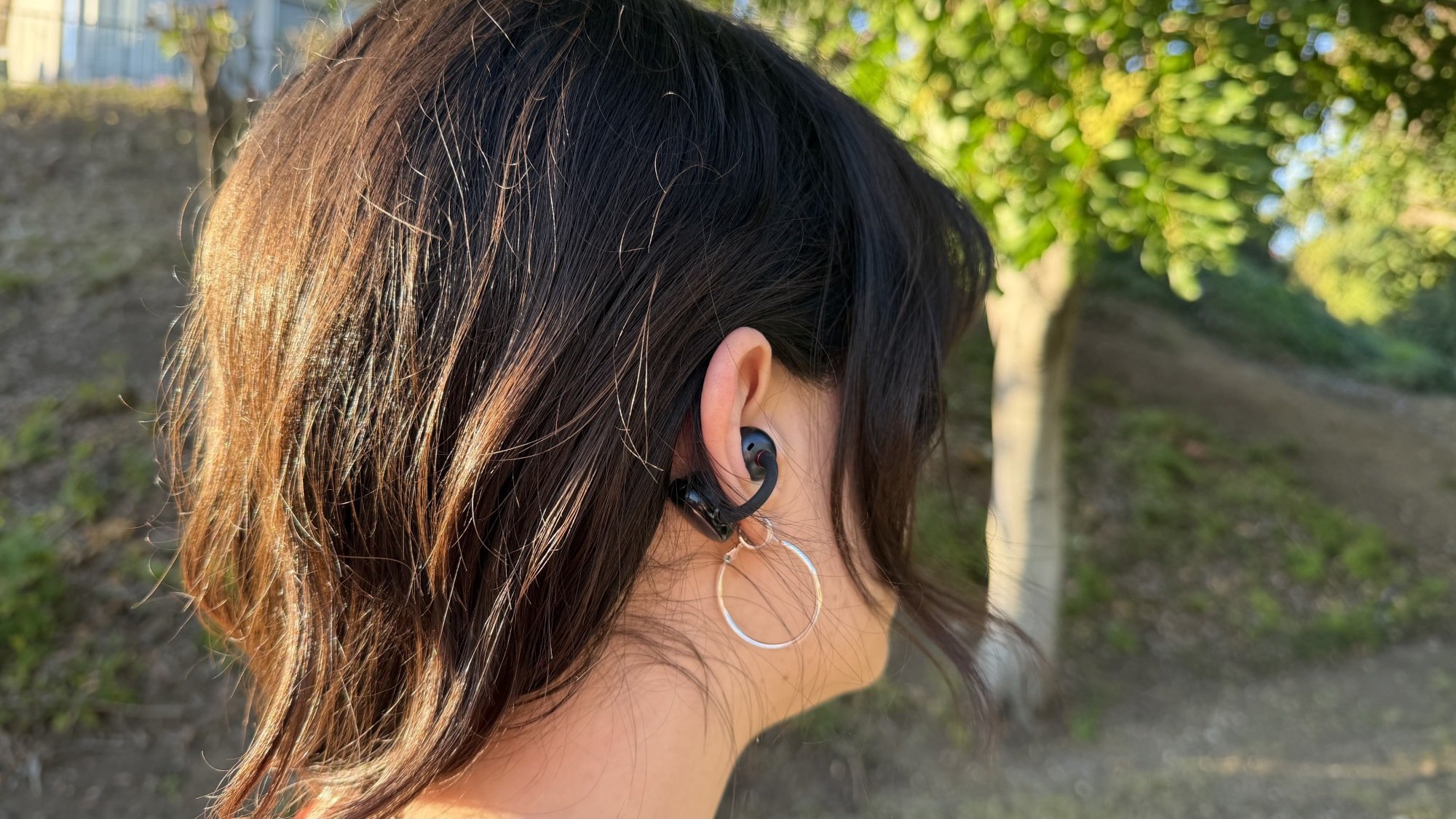 person standing outside wearing black cuff open earbuds and two hoop earrings