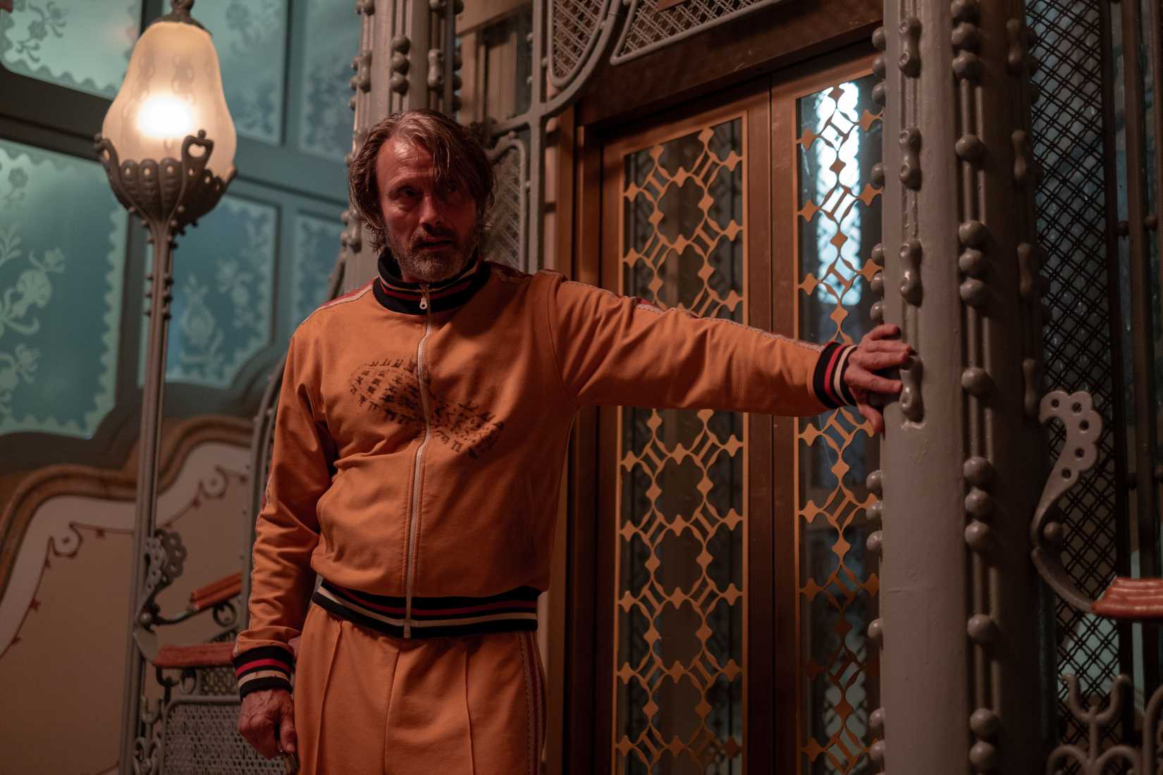 An image from Bryan Fuller's Dust Bunny. Mads Mikkelsen wears a yellow tracksuit and leans against an elevator.